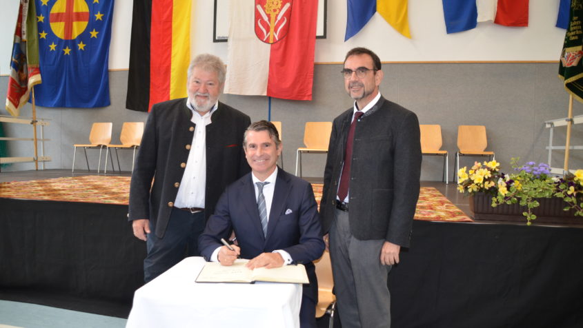 Europaminister Eric Beißwenger (Mitte) trägt sich im Beisein des Bürgermeisters der Gemeinde Niederrieden, Michael Büchler (links), und MdL Klaus Holetschek (rechts) in das Gästebuch der Gemeinde Niederrieden ein. © Gemeinde Niederrieden